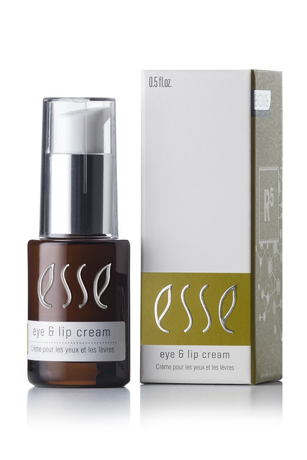 A brown bottle of Esse Eye & Lip Cream with a white pump dispenser is displayed next to its white and green box packaging. The text on the bottle and box reads "Esse Eye & Lip Cream - Crème pour les yeux et les lèvres." The bottle contains 0.5 fl oz of product.