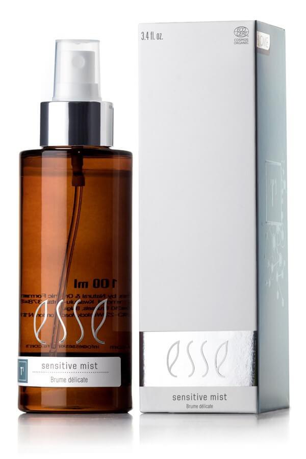 A 100ml brown bottle of "Esse Sensitive Mist," topped with a white spray nozzle, is placed beside a white rectangular box bearing the same product name. The box features a silver band near the bottom and text specifying it as a sensitive mist for delicate skin.
